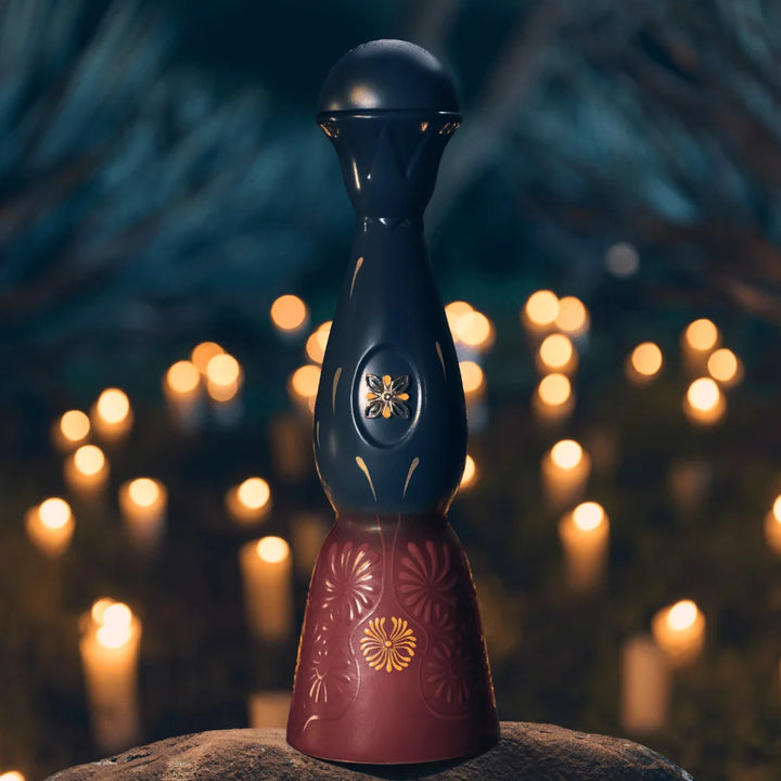 Decorative tequila bottle with dark blue upper, burgundy lower, and gold flower emblem