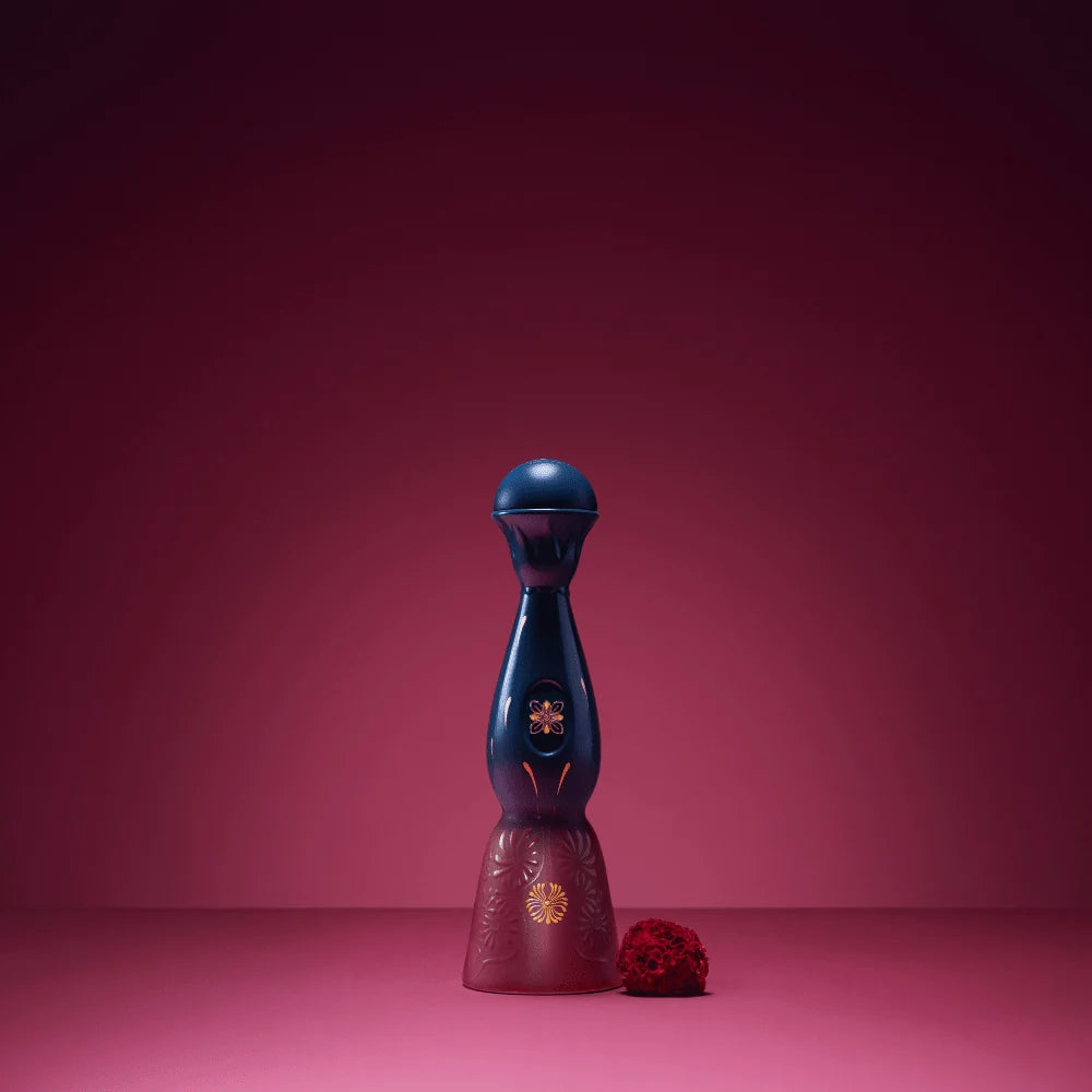 Tequila bottle with dark blue top, burgundy base, gold flower; small red decoration nearby