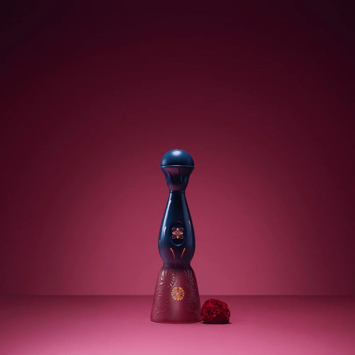 Tequila bottle with dark blue top, burgundy base, gold flower; small red decoration nearby