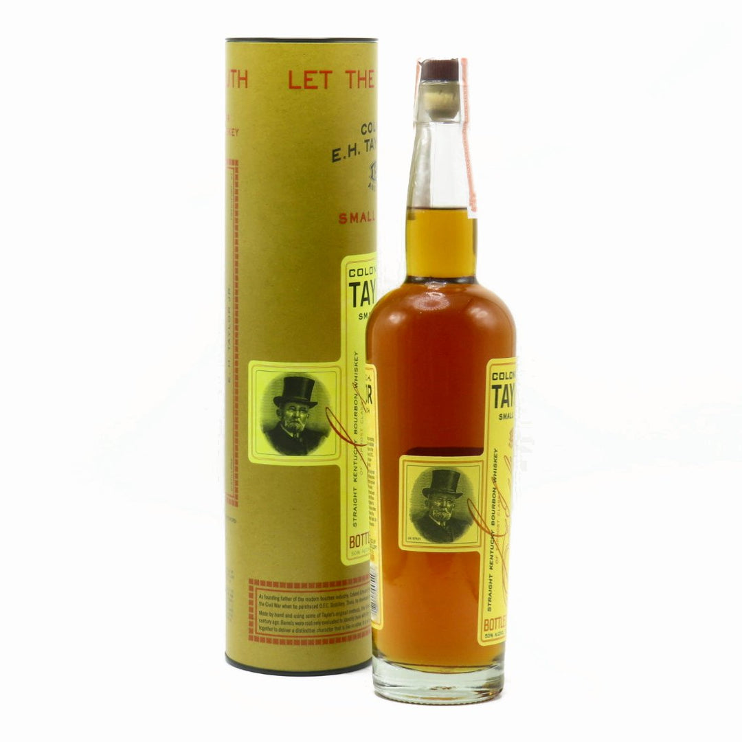 Small-batch bourbon whiskey bottle with label, gold liquid, beside tall carton sleeve